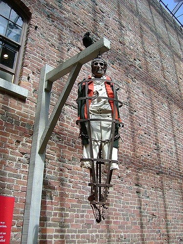 A skeleton in a metal cage hanging from a wooden post against a brick wall