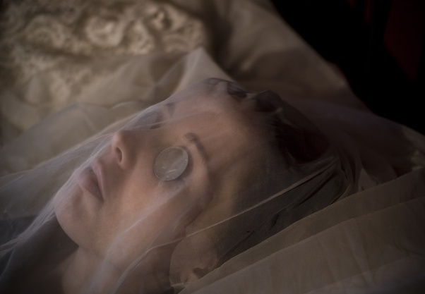 A person lying down with a coin placed over the eye, covered by a veil